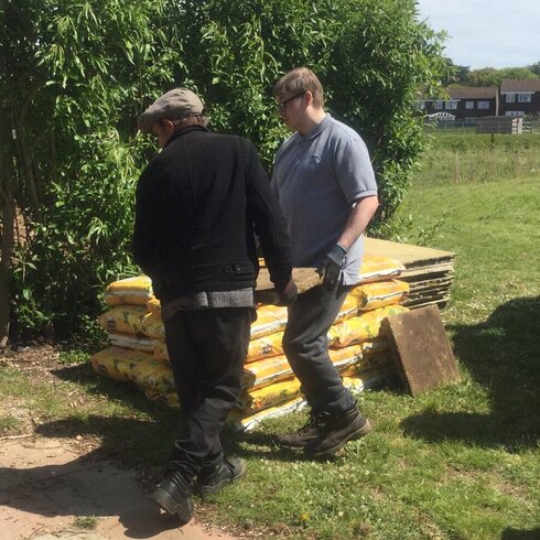 Two gardeners carrying a paving slab.